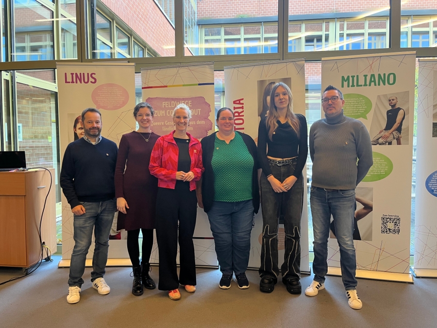 Laden herzlich zum Besuch der Ausstellung ein:  Rene Weitzenbürger (stellvertretenden Schulleitung Ludwig Erhard Berufskolleg); Nathalie Eikmeier (Schulsozialarbeit Ludwig Erhard Berufskolleg); Jana Hansjürgen (Leitung Landesfachstelle blick* zu LSBTIQ+ Strukturen im ländlichen Raum); Verena Fromme (Schulsozialarbeit Ludwig Erhard Berufskolleg); Victoria Drüke (Teilnehmerin der Ausstellung und Queere Beratung); Carlos Tomé (Kreisjugendamt Paderborn). © Naomi Grützbach